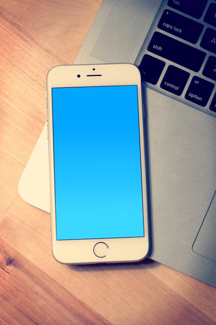 Elegant Apple iPhone with a blank screen placed next to a MacBook on a wooden desk.